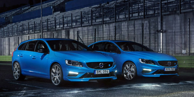 Two blue Volvo station wagons parked side-by-side at the start line on a race track at night.