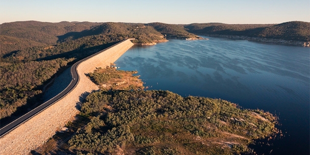 car travels along a winding road on the top of Copeton Dam with water to the right and forest to the right