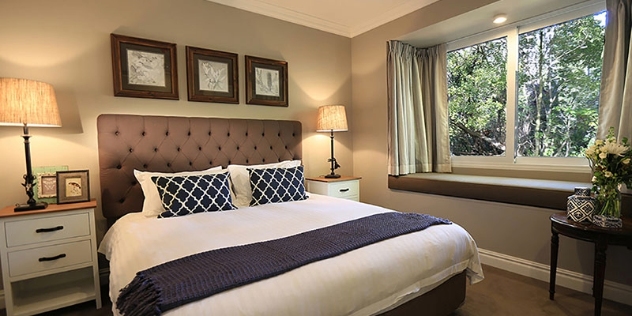 stylish hotel bedroom with comfortable looking bed with cream coverlet, cushions and a window seat