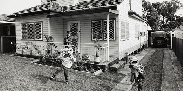 black and white photo of children in front of a house with chinese new year dragon masks